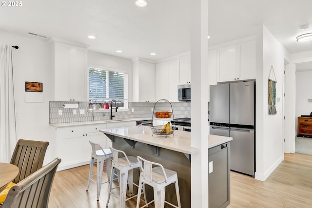 kitchen with appliances with stainless steel finishes, a sink, light wood-style flooring, backsplash, and recessed lighting