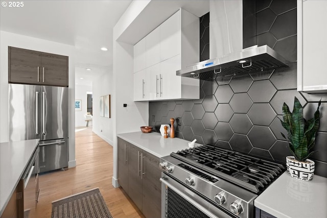 kitchen with white cabinets, light wood-style flooring, appliances with stainless steel finishes, light countertops, and wall chimney range hood