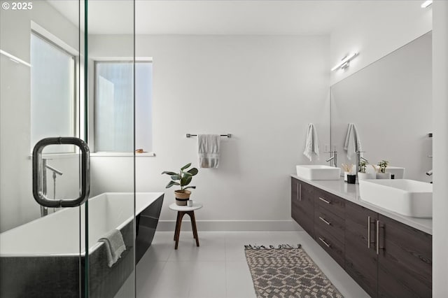 bathroom with a freestanding bath, tile patterned floors, a sink, and baseboards