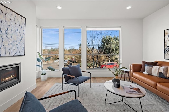 living area with a glass covered fireplace, baseboards, recessed lighting, and wood finished floors