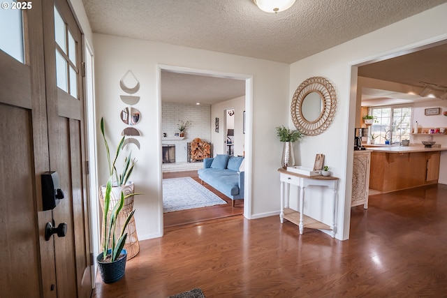 entryway featuring a fireplace, wood finished floors, baseboards, and a textured ceiling