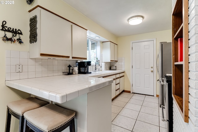 kitchen featuring sink, a breakfast bar, tile counters, white cabinets, and kitchen peninsula