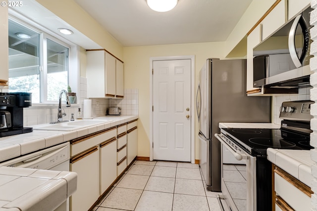 kitchen featuring sink, white cabinetry, backsplash, stainless steel appliances, and tile counters