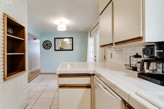 kitchen featuring light tile patterned floors, dishwasher, white cabinetry, backsplash, and tile counters