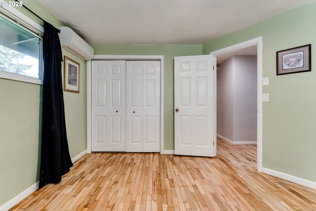 unfurnished bedroom featuring a closet, a wall mounted air conditioner, and light hardwood / wood-style flooring