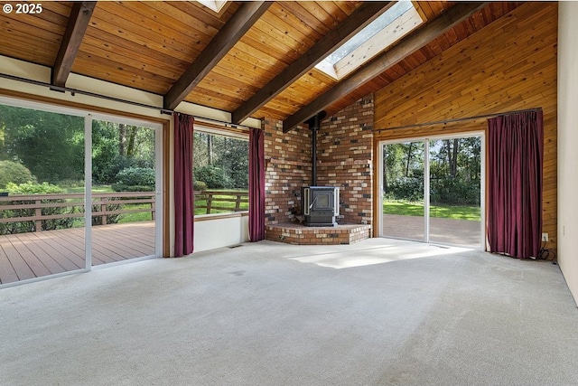 unfurnished living room featuring a skylight, wooden ceiling, a wood stove, carpet flooring, and beam ceiling