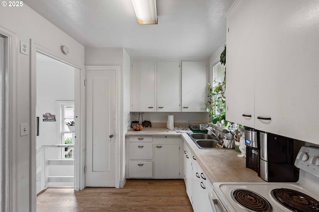 kitchen with a sink, white cabinetry, light countertops, and electric range