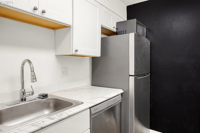 kitchen featuring appliances with stainless steel finishes, light stone counters, white cabinetry, and sink