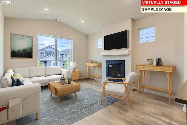 living room featuring lofted ceiling, a glass covered fireplace, baseboards, and wood finished floors