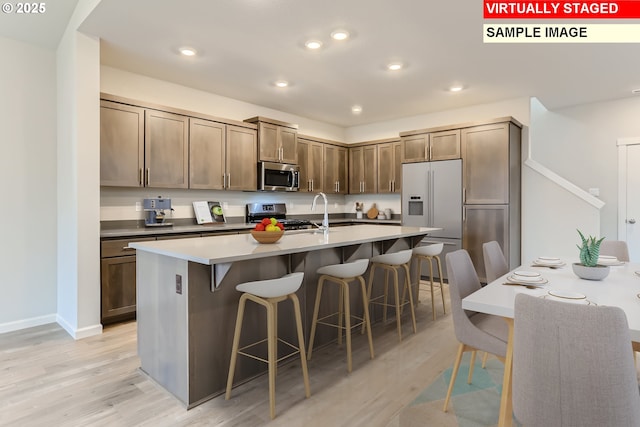 kitchen featuring stainless steel appliances, light wood finished floors, a kitchen bar, and a kitchen island with sink