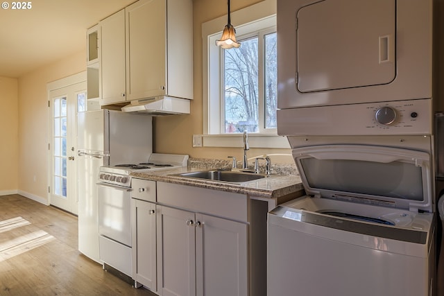 kitchen featuring white electric range, white cabinetry, sink, stacked washer and dryer, and hanging light fixtures