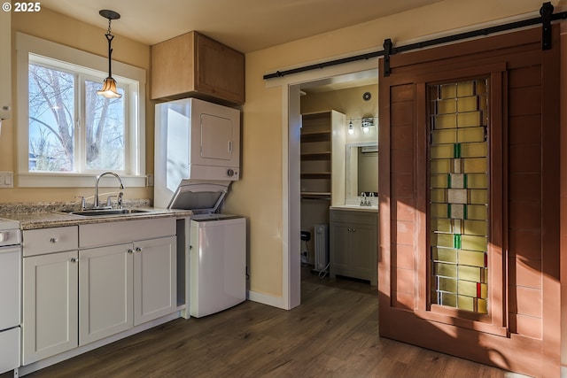 kitchen with stacked washer and clothes dryer, sink, hanging light fixtures, a barn door, and white cabinets