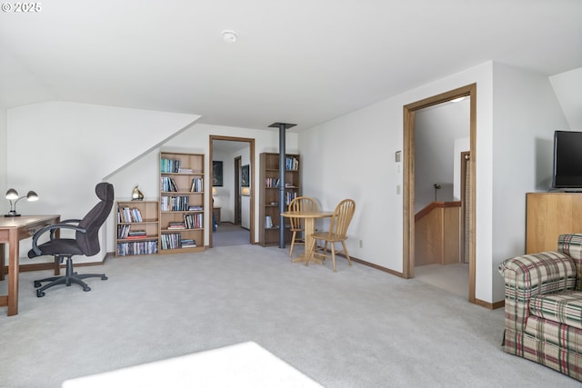 carpeted home office featuring vaulted ceiling and a wood stove