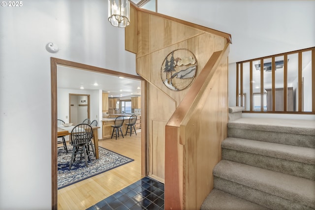 stairway with a high ceiling, wood-type flooring, and a notable chandelier