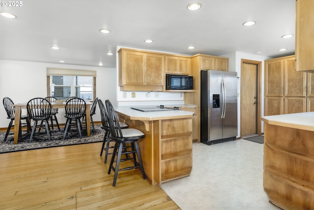 kitchen with stainless steel fridge with ice dispenser, a kitchen breakfast bar, black microwave, and light wood-type flooring