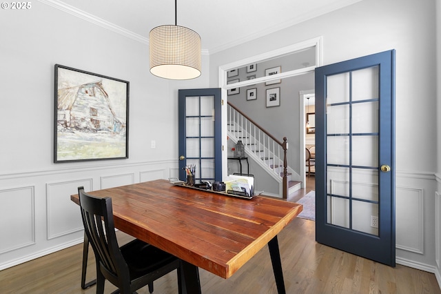 dining area with ornamental molding, a decorative wall, wood finished floors, stairway, and a wainscoted wall