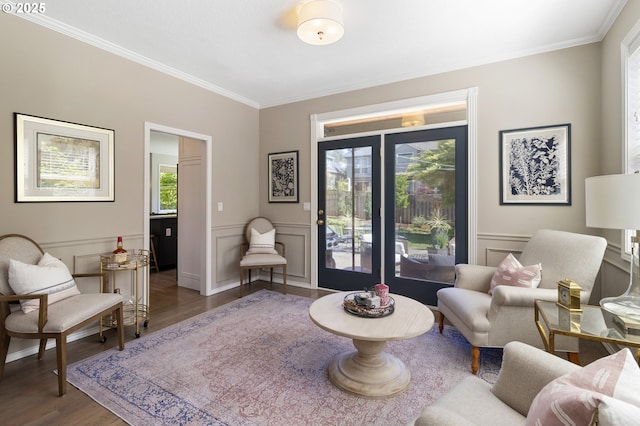 living area with ornamental molding, wood finished floors, a decorative wall, and a wainscoted wall