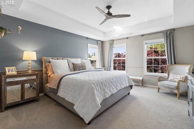 carpeted bedroom featuring a tray ceiling, baseboards, and a ceiling fan