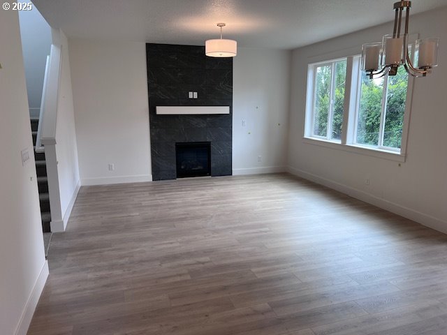 unfurnished living room with wood finished floors, a chandelier, baseboards, and a premium fireplace