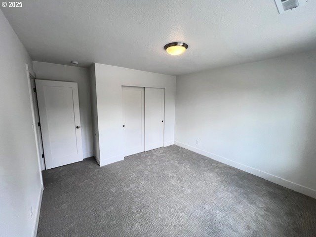unfurnished bedroom featuring dark colored carpet, a closet, baseboards, and a textured ceiling