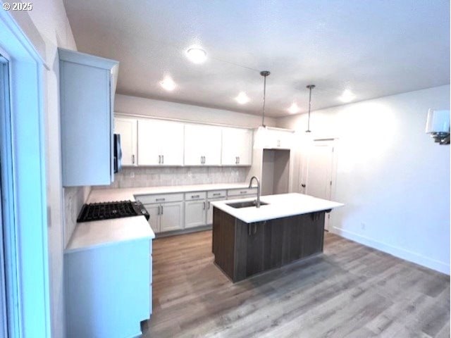 kitchen featuring a sink, a center island with sink, baseboards, light wood-style flooring, and light countertops