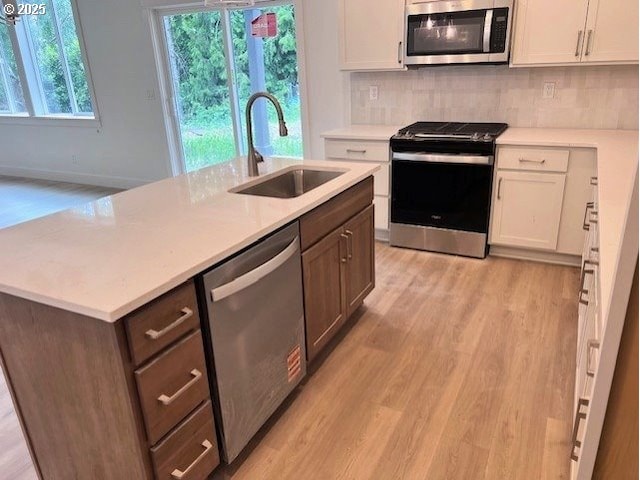 kitchen with stainless steel appliances, a sink, light wood-style flooring, white cabinetry, and light countertops