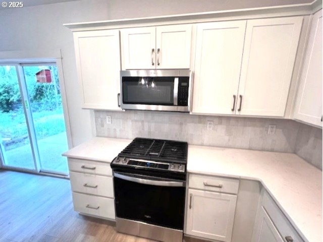 kitchen with stainless steel microwave, gas range oven, light wood-style floors, backsplash, and light countertops