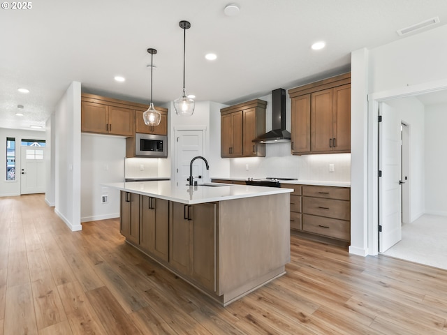 kitchen with wall chimney exhaust hood, tasteful backsplash, visible vents, stainless steel microwave, and a sink