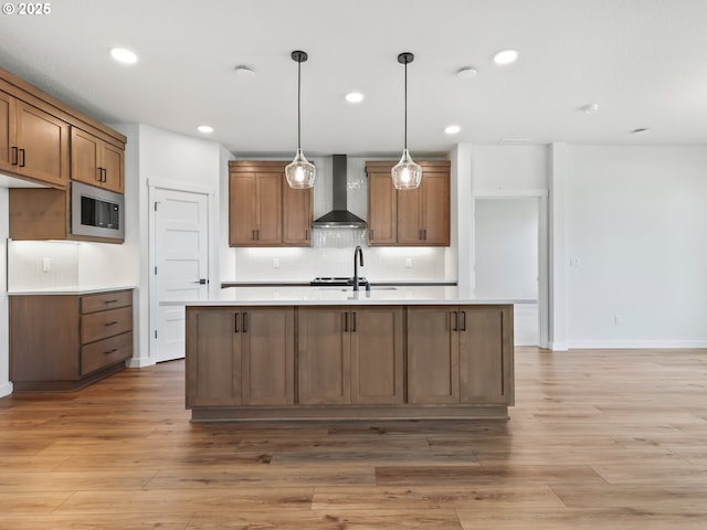 kitchen with stainless steel microwave, tasteful backsplash, light wood-type flooring, wall chimney range hood, and brown cabinetry