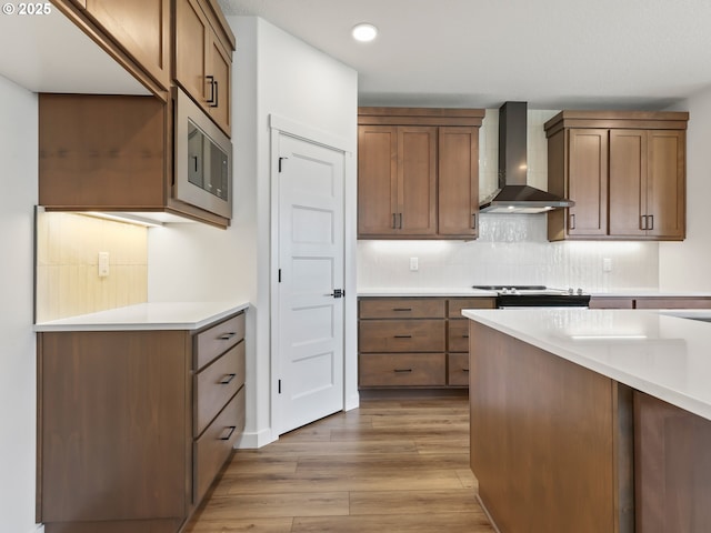 kitchen featuring stainless steel microwave, tasteful backsplash, light countertops, wall chimney exhaust hood, and wood finished floors