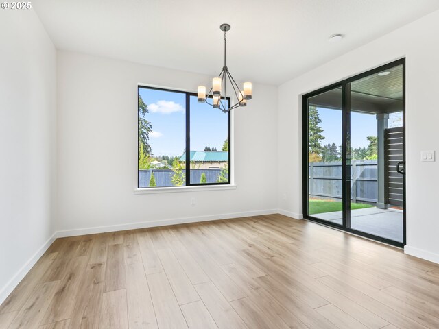 spare room with a notable chandelier, baseboards, and light wood-style flooring