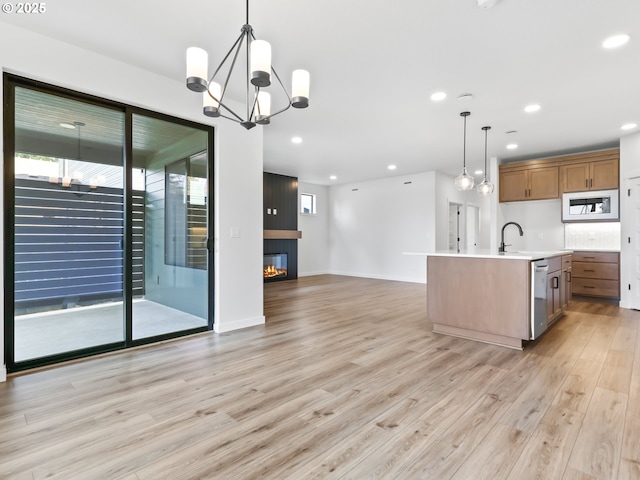 kitchen featuring white microwave, open floor plan, light countertops, stainless steel dishwasher, and light wood finished floors