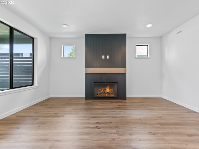 unfurnished living room featuring wood finished floors, baseboards, a large fireplace, and a wealth of natural light