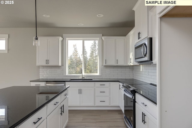 kitchen with hanging light fixtures, a wealth of natural light, stainless steel microwave, and white cabinetry