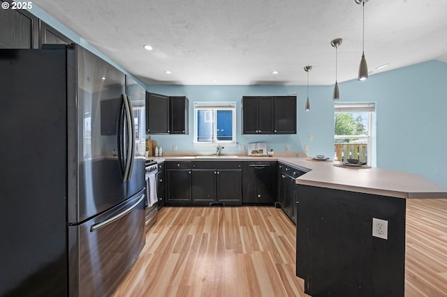kitchen featuring a sink, appliances with stainless steel finishes, light wood finished floors, and a peninsula