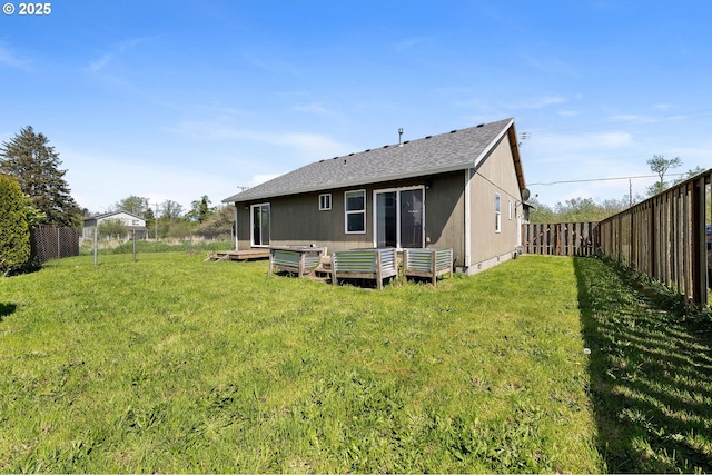 rear view of property featuring a yard, a wooden deck, a fenced backyard, and roof with shingles
