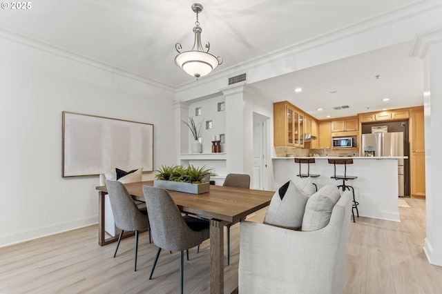 dining area featuring decorative columns, crown molding, sink, and light wood-type flooring