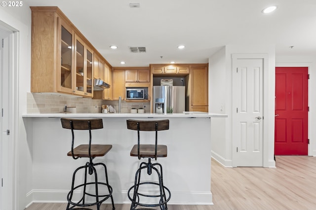 kitchen featuring a kitchen bar, light wood-type flooring, stainless steel refrigerator with ice dispenser, and tasteful backsplash