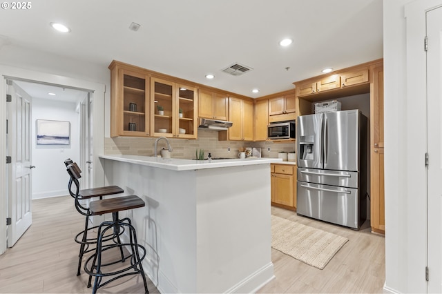 kitchen featuring light hardwood / wood-style floors, a kitchen bar, kitchen peninsula, and appliances with stainless steel finishes