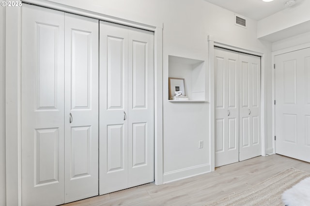 unfurnished bedroom with multiple closets and light wood-type flooring