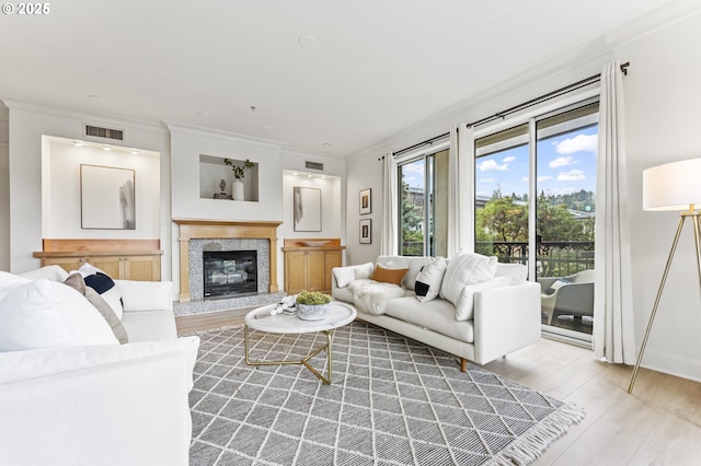 living room with a high end fireplace, light wood-type flooring, and ornamental molding