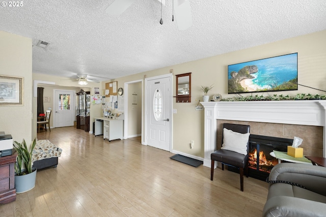 living room with ceiling fan, a textured ceiling, a fireplace, light wood-style flooring, and baseboards