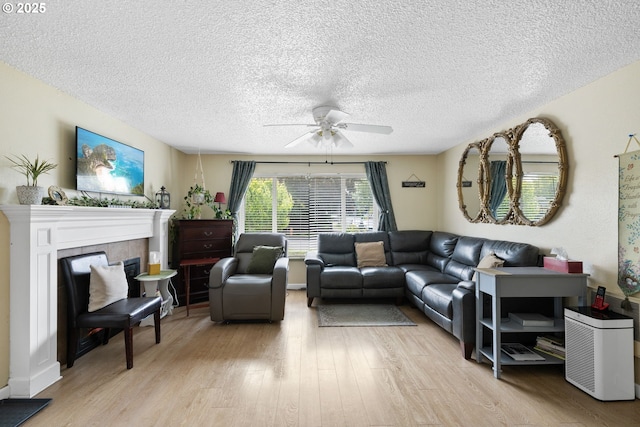 living room featuring ceiling fan, light wood-style floors, a textured ceiling, and a tile fireplace