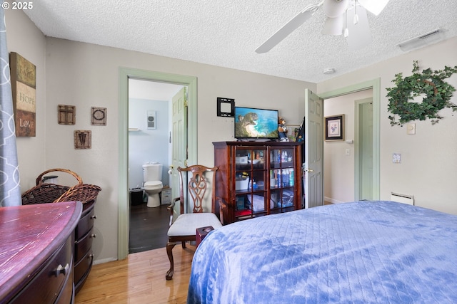 bedroom featuring light wood-style floors, a textured ceiling, connected bathroom, and a ceiling fan