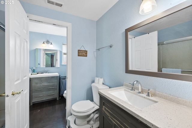 full bath featuring toilet, vanity, a shower with door, wood finished floors, and a textured wall