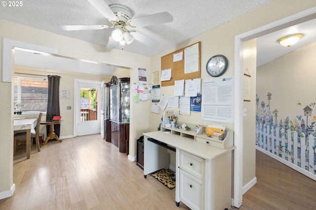 hallway with light wood-type flooring, a desk, baseboards, and a textured ceiling