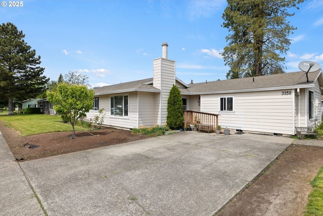 back of property featuring a lawn, a chimney, roof with shingles, and concrete driveway