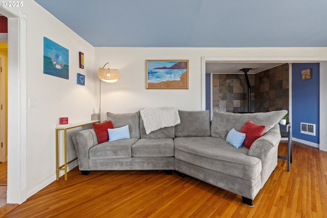 living area with a wood stove, visible vents, baseboards, and wood finished floors