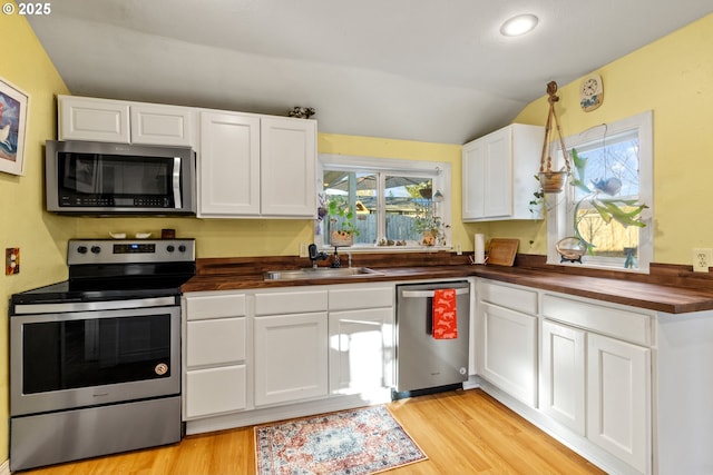 kitchen featuring appliances with stainless steel finishes, a sink, butcher block counters, and white cabinetry