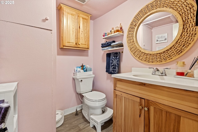 half bath featuring visible vents, baseboards, toilet, wood finished floors, and vanity